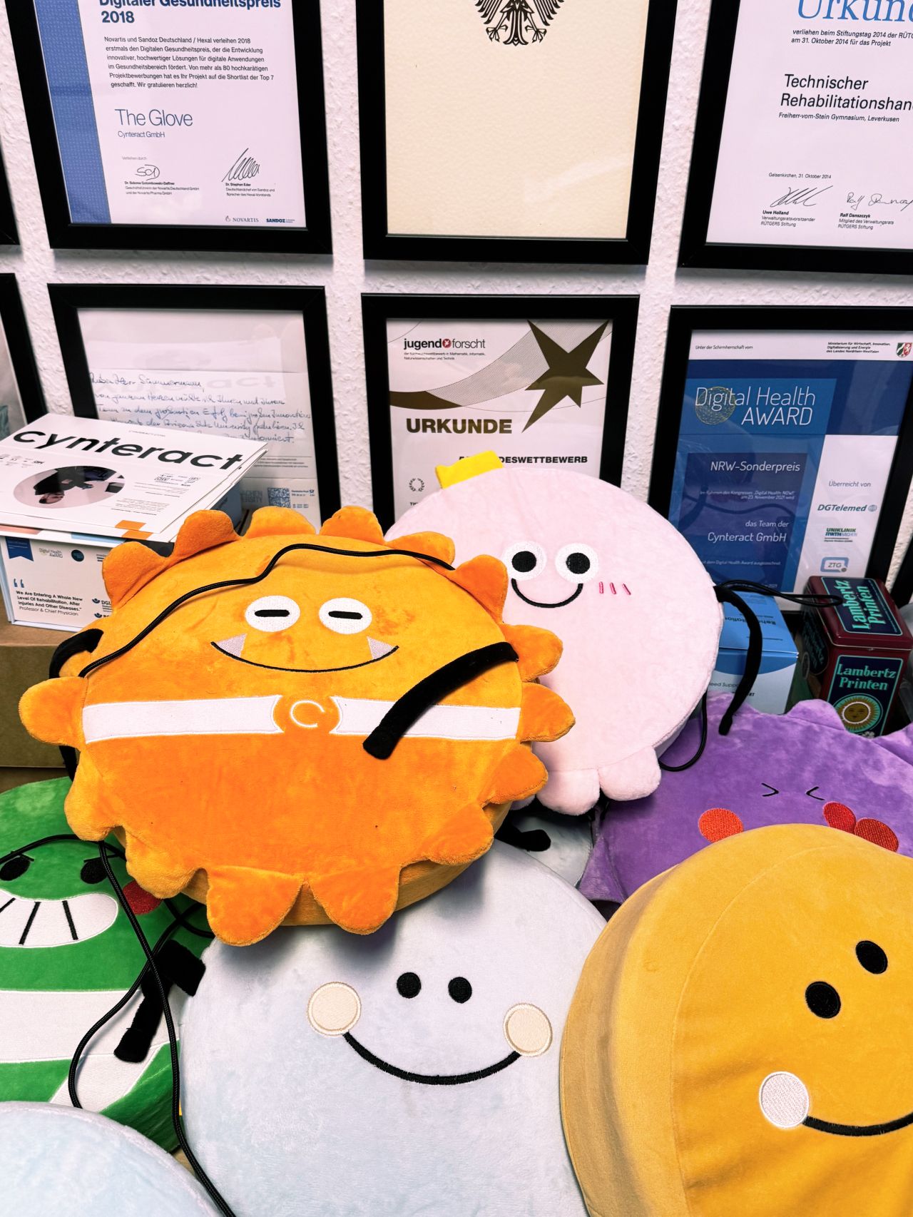 A collection of Cynteract Cushions in various colors, displayed in front of the company's award wall