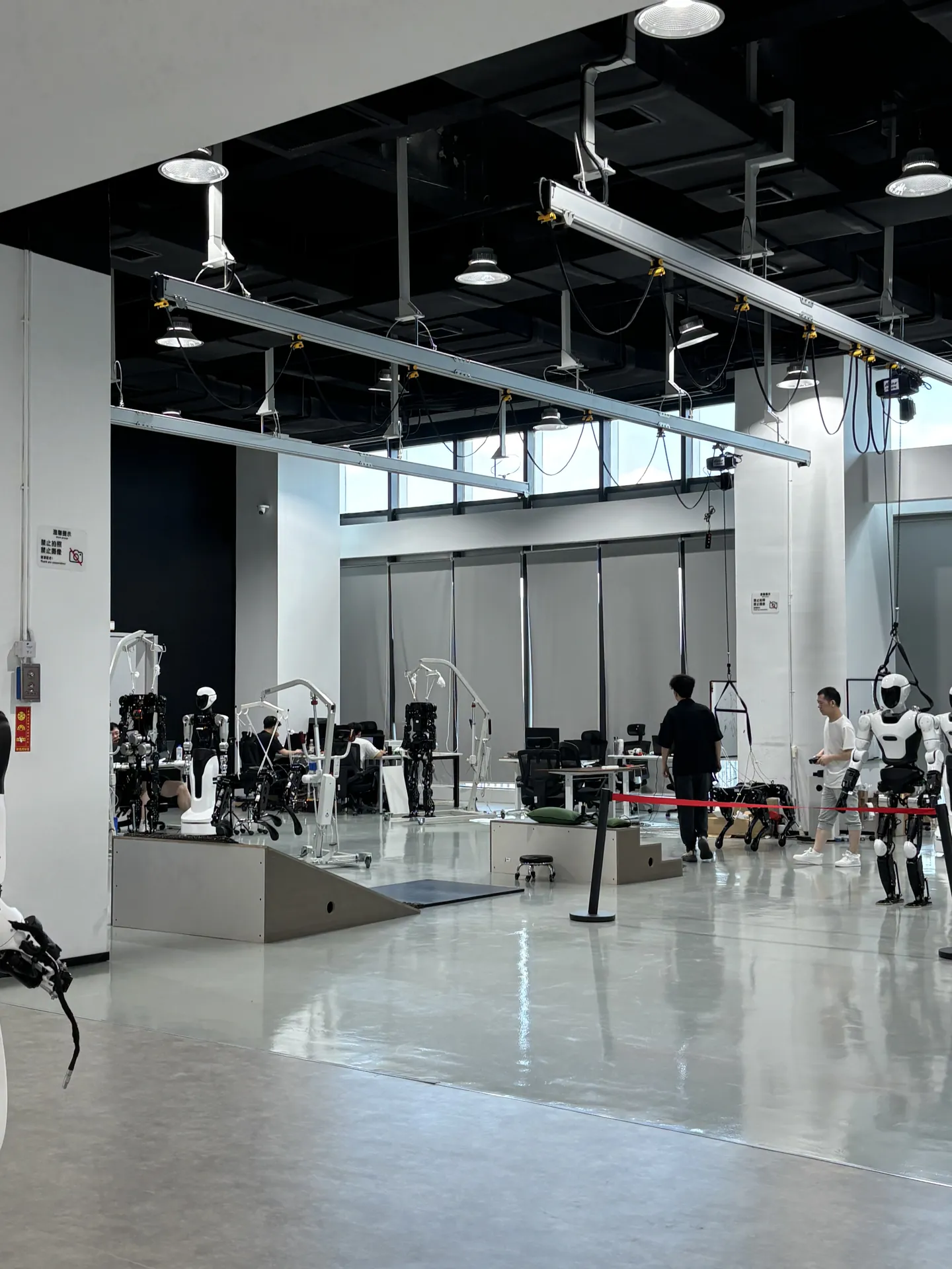 A humanoid robot lab with several white humanoid robots and engineers working at desks