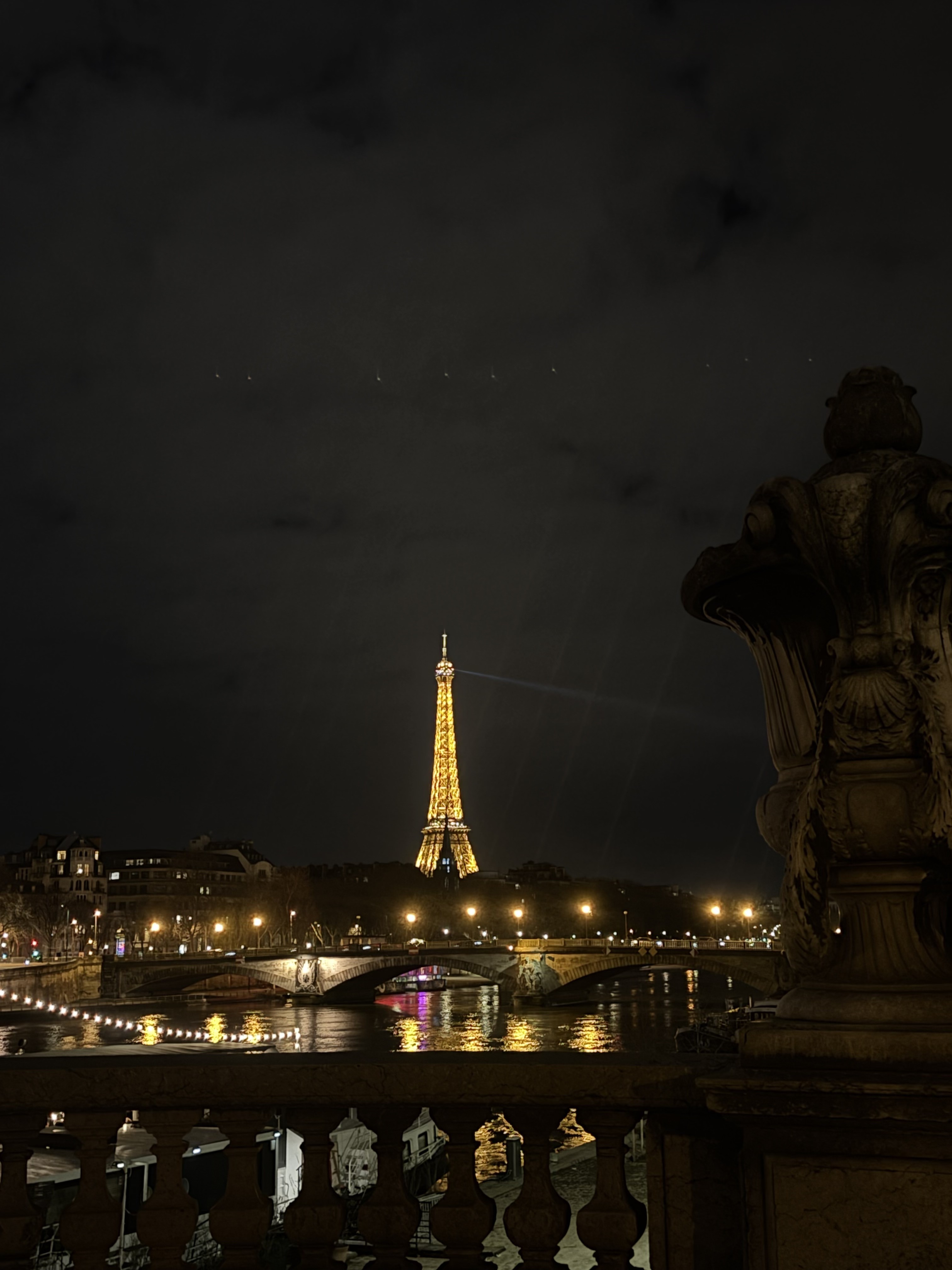 The Eiffel Tower lit up at night, viewed from a bridge over the Seine